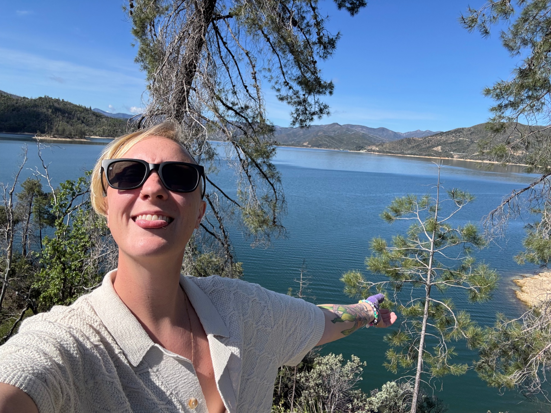 Smiling under a tree with a lake and mountains behind